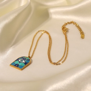 Detail of a golden Hamsa necklace with blue and green enamel and evil eye charm on silk