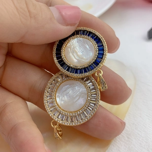 Golden Virgin Mary shell pendants with blue and clear zircon crystals held by fingers
