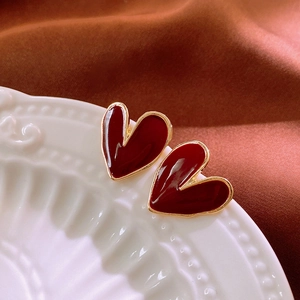 Macro detail of red enamel heart earrings with gold trim on white vintage plate