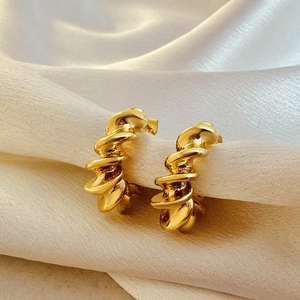 Detailed view of gold twisted croissant earrings on white silk fabric with elegant lighting