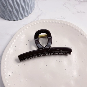 Detailed view of a glossy dark brown hair claw clip with a durable gold metal spring