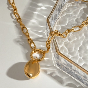 Elegant gold plated stainless steel necklace with organic resin pearl pendant on glass