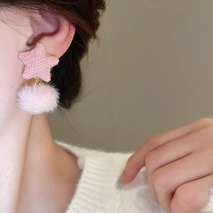 Detail eines rosa gestrickten Sterns und Plüschkugel-Ohrrings an einem Modell