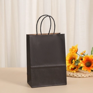 Minimalist black paper gift bag with rope handles on a warm decorative background