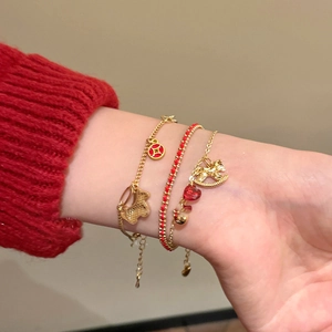 Wrist close-up of a three-piece gold and red lucky charm bracelet set with horse pendant