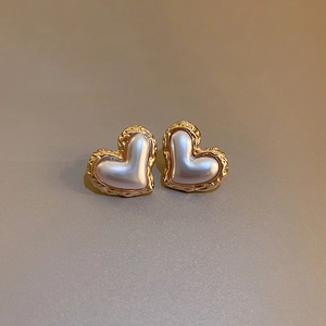 Close-up of golden textured heart stud earrings with glossy pearl center on clean background