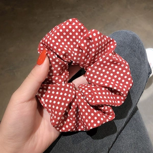 Detail of red and white polka dot scrunchie held against denim fabric background