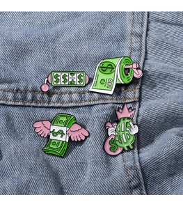 Close-up of creative dollar themed enamel pins attached to a blue denim jacket pocket