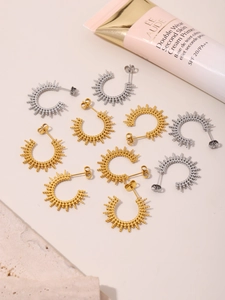 Detail view of gold and silver sunburst bead C-shape earrings on a neutral stone surface