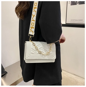 Detail of white quilted crossbody bag with golden flower chain and wide fabric strap