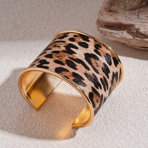 Macro detail of wide leopard print open bangle with golden metal edges on a stone background