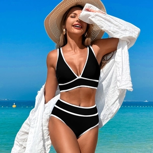 Detail of high-waist black bikini set with white stripes on a sunny tropical beach
