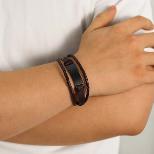 Close-up of a multi-layer dark brown braided leather bracelet with a black metal bar