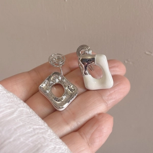 Silver geometric square earrings with white enamel detail held for size reference