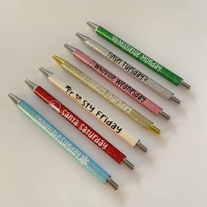 Detailed view of seven colorful glitter pens with holiday phrases for Christmas gift
