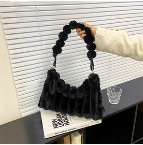 Detail of black faux fur handbag featuring unique wave pleats and plush ball handle