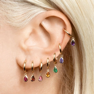 Macro shot of colorful pear-cut zircon earrings and ear cuffs on a model ear