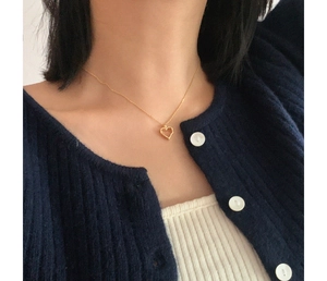 Close-up of minimalist gold hollow heart necklace worn by a model on a blue knit sweater