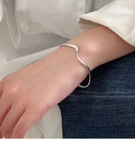 Primo piano di un bracciale rigido a onde d'argento minimalista indossato al polso