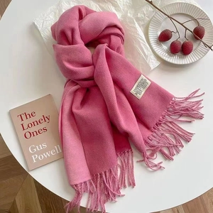 Pink cashmere feel scarf with fringe tassels displayed on a table with lifestyle props