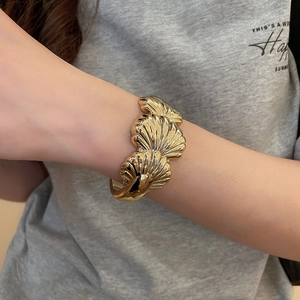 Macro detail of golden open cuff bracelet with overlapping shell-shaped textured metal