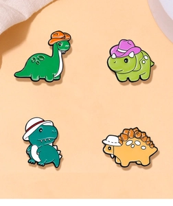 Detailed top view of four colorful enamel dinosaur pins with cute hats on peach surface