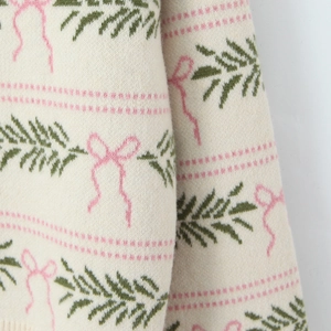 Festive cream knit sweater with pink bows and green pine patterns in close-up view