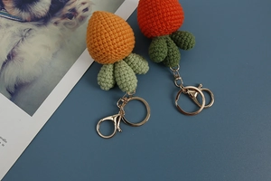 Macro detail of two handmade crochet carrot pendants with gold metal keychains