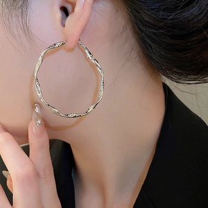Nahaufnahme eines silbernen gedrehten Creolen-Ohrrings für Damen im minimalistischen Stil