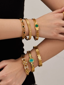 Detail of stacked gold stainless steel bracelets with triangle patterns and green stones