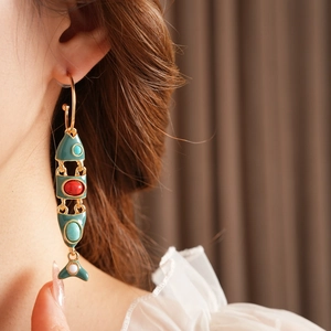 Detailed shot of vintage gold fish earring with green and red enamel scales on model