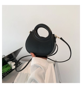 Detail of black saddle bag with wavy stripe embossing and elegant gold metal buckle