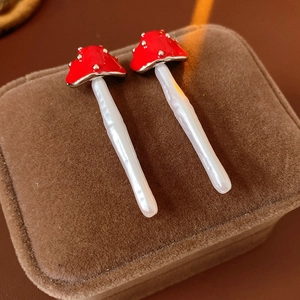 Detailed close-up of red mushroom earrings with white spots on a brown velvet box