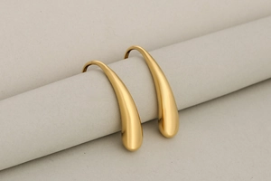 Macro detail of high-polished golden teardrop earrings on a soft minimalist background