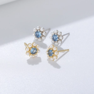 Macro shot of silver and gold flower earrings with blue zircon and small pearls