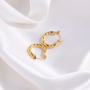 Detail of golden bamboo textured hoop earrings on elegant white silk fabric