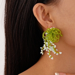 Close-up of handmade green and white beaded floral earrings on model ear for summer