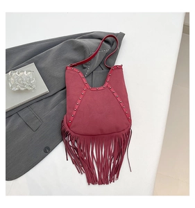 Close-up of a burgundy suede tassel bag featuring rivets and an embossed sun motif