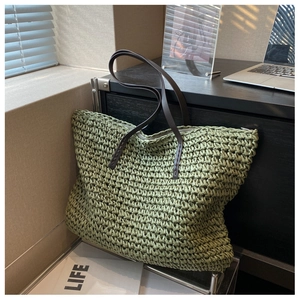 Detail of green woven tote bag with brown leather handles on a sunlit wooden table