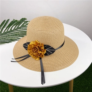 Detail of handwoven beige straw hat with large yellow fabric flower and black silk ribbon