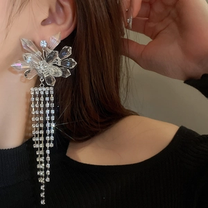 Détail de boucles d'oreilles fleur en cristal argenté et longues franges strass
