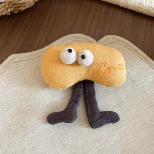 Detail of yellow plush biscuit brooch with big eyes and embroidered lettering on linen