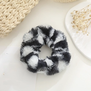 Detail of plush cow print scrunchie with soft faux fur texture on a minimalist desk