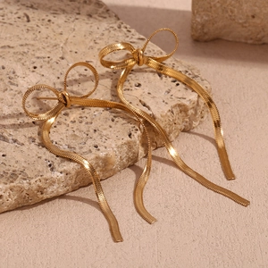 Detailed macro of 18K gold plated bowknot tassel earrings on natural stone background