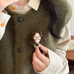 Dettaglio di una spilla a bambola fatta a mano con occhiali su gilet di maglia