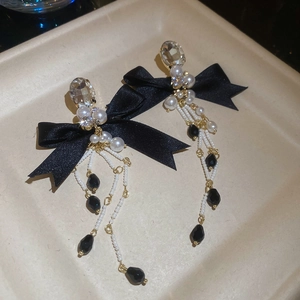 Close-up of elegant bow earrings with long pearl tassels and crystal stud on a beige tray