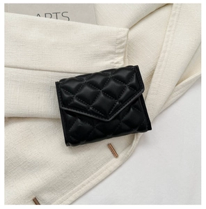 Close-up of black quilted PU leather small square bag on a beige blazer background