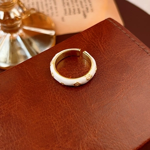 Dettaglio di un anello a fiori placcato oro con smalto bianco su fondo in pelle scura