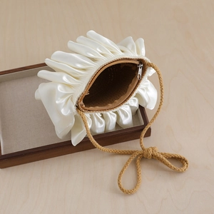 Close-up of cream pleated satin shoulder bag with woven strap and straw lining