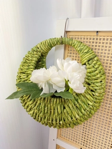 Close-up of handmade green woven wall basket featuring white peonies and leaf detail